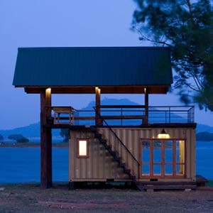 Lakeside shipping container cabana with wooden wrap-around decks and overhanging steel roof