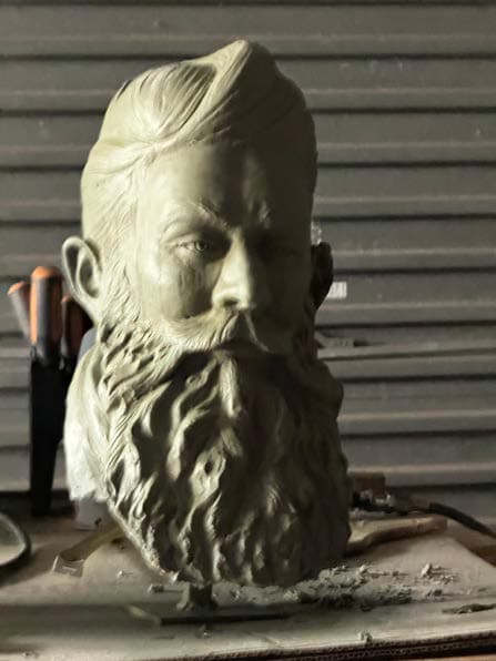 Two portrait sculptures of Ned Kelly placed side-by-side: one in iron mask, one showing facial features